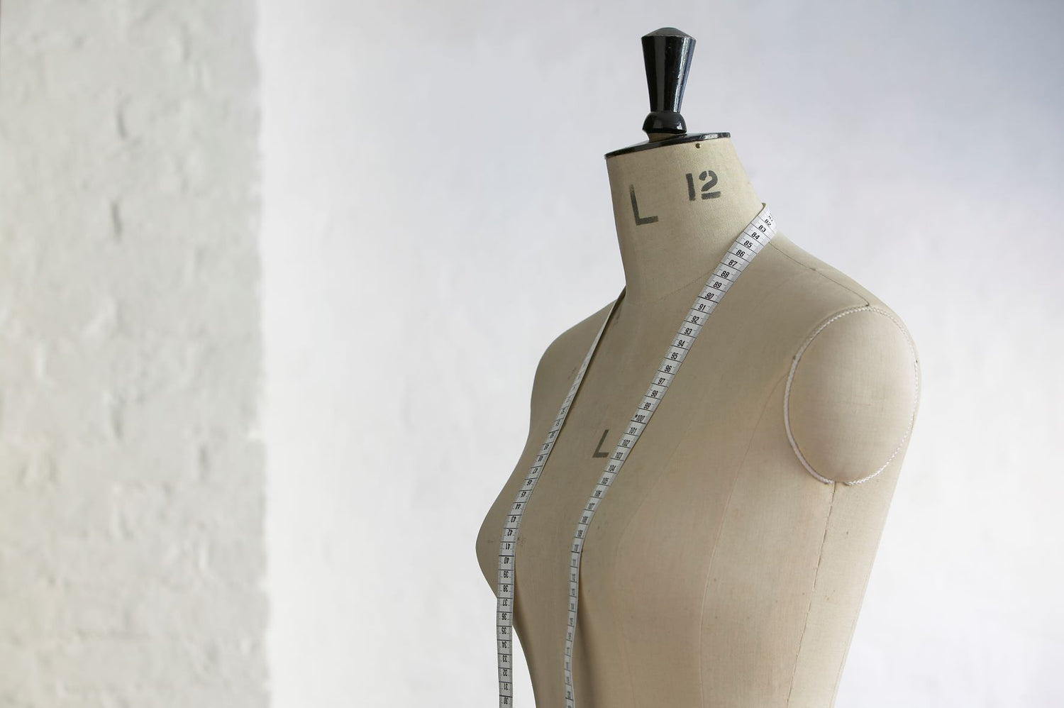 Schneiderpuppe mit Maßband vor weißer Wand