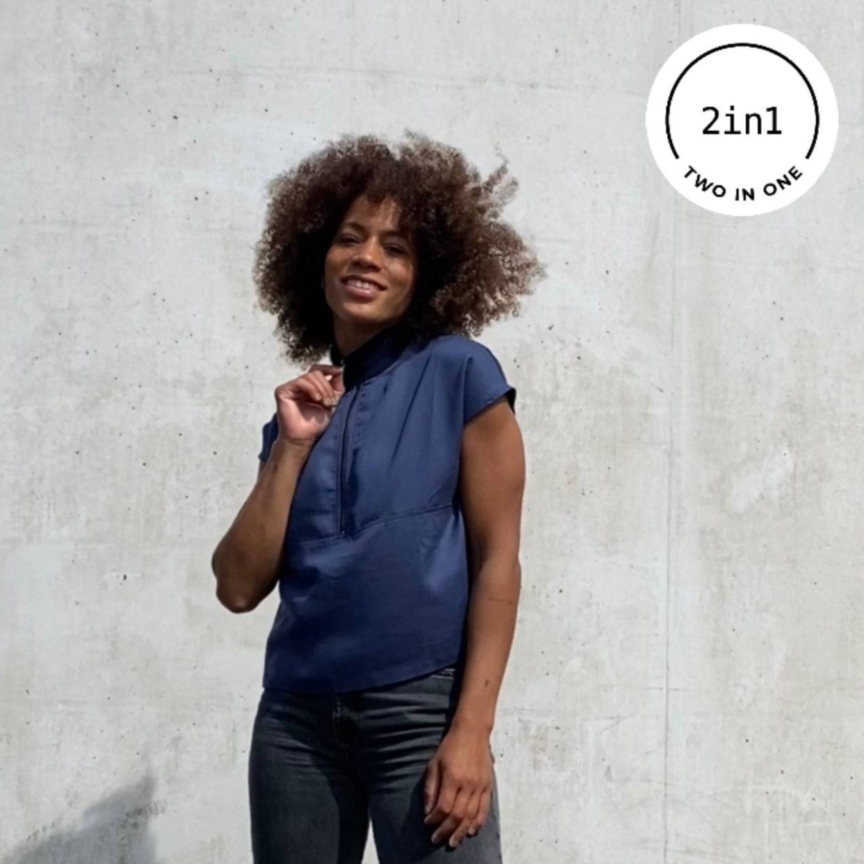 Frau mit indigo-farbener Bluse mit Reißverschluss vor grauer Betonwand mit 2IN1-Icon