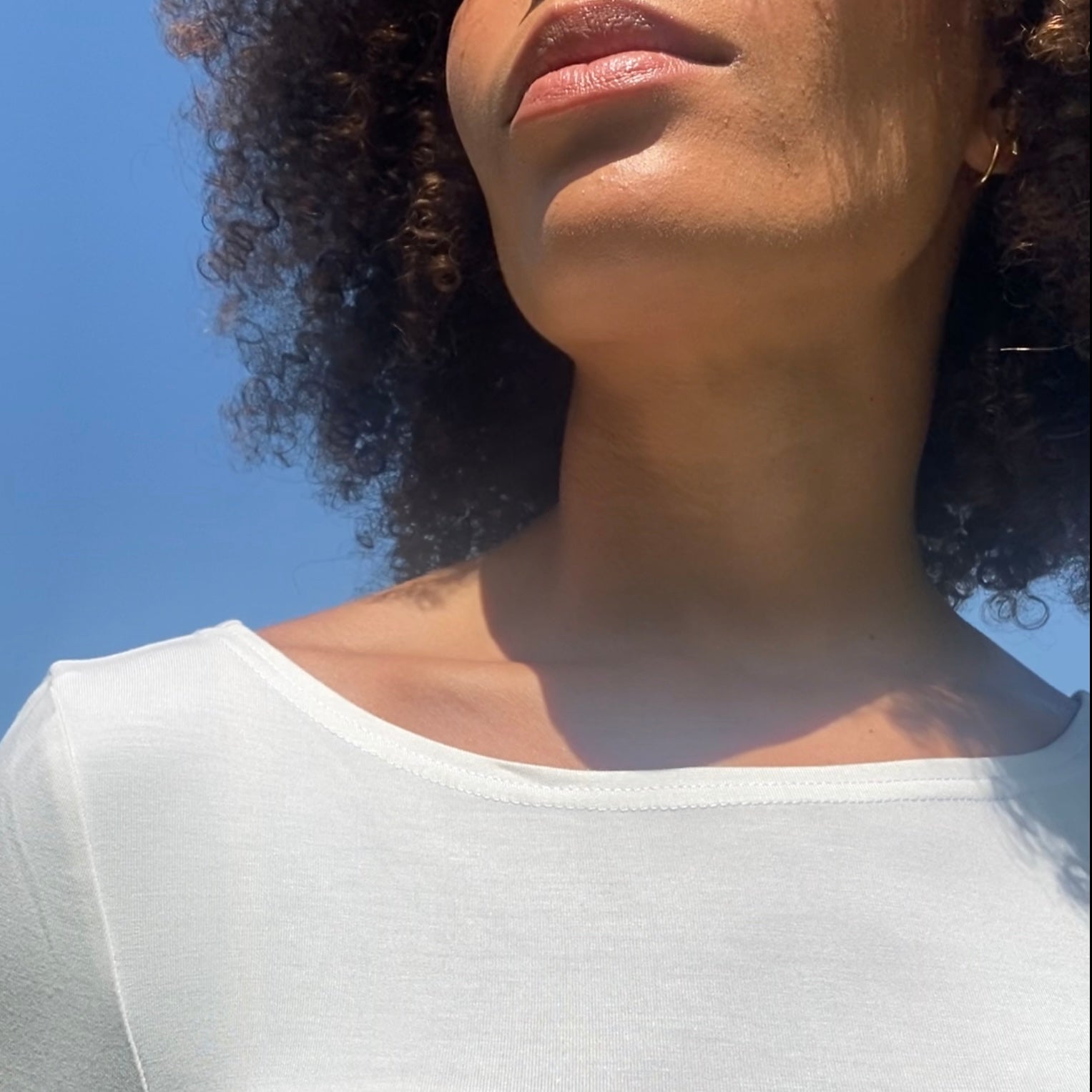 Detail von Ausschnitt eines Ballerina T in ecru an Frau vor blauem Himmel