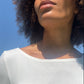 Detail von Ausschnitt eines Ballerina T in ecru an Frau vor blauem Himmel