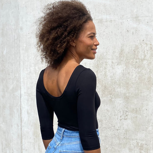 Rückenansicht von Frau mit schwarzem Ballerina T vor grauer Betonwand stehend