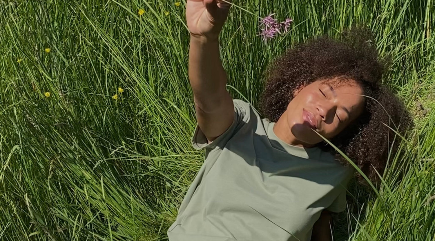 Frau auf RÜcken im Gras liegend mit Blume und grünem T-Shirt