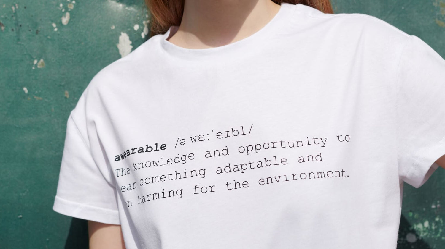 Ausschnitt zeigt Frau vor grünem Hintergrund bekleidet mit einem weißem T-Shirt, das einen schwarzem Schriftzug trägt, der awearable definiert