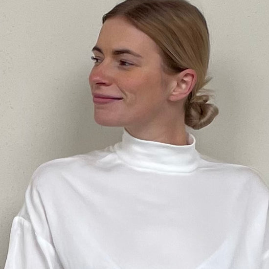 Seitenansicht einer blonden Frau mit weißer Bluse vor beigem Hintergrund