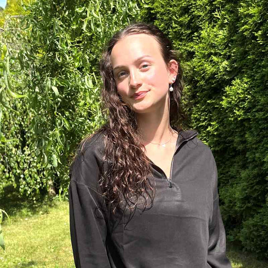 Frau mit langen braunene Haaren in Natur mit schwarzer Bluse